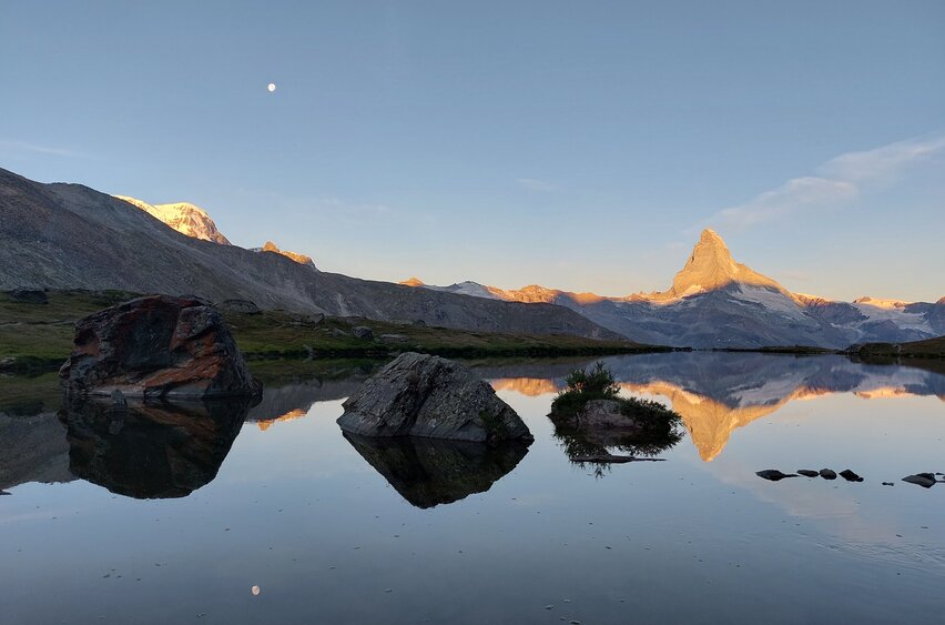 The Matterhorn is reflected in Lake Stelli. The peaks around the Matterhorn are equally illuminated by the first rays of sunshine | © Zermatt Bergbahnen