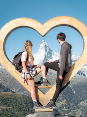 Fotopoint Holzherz auf Blauherd im Sommer. Ein Paar sitzt im Holzherz und sieht zum Matterhorn | © Basic Home Production 